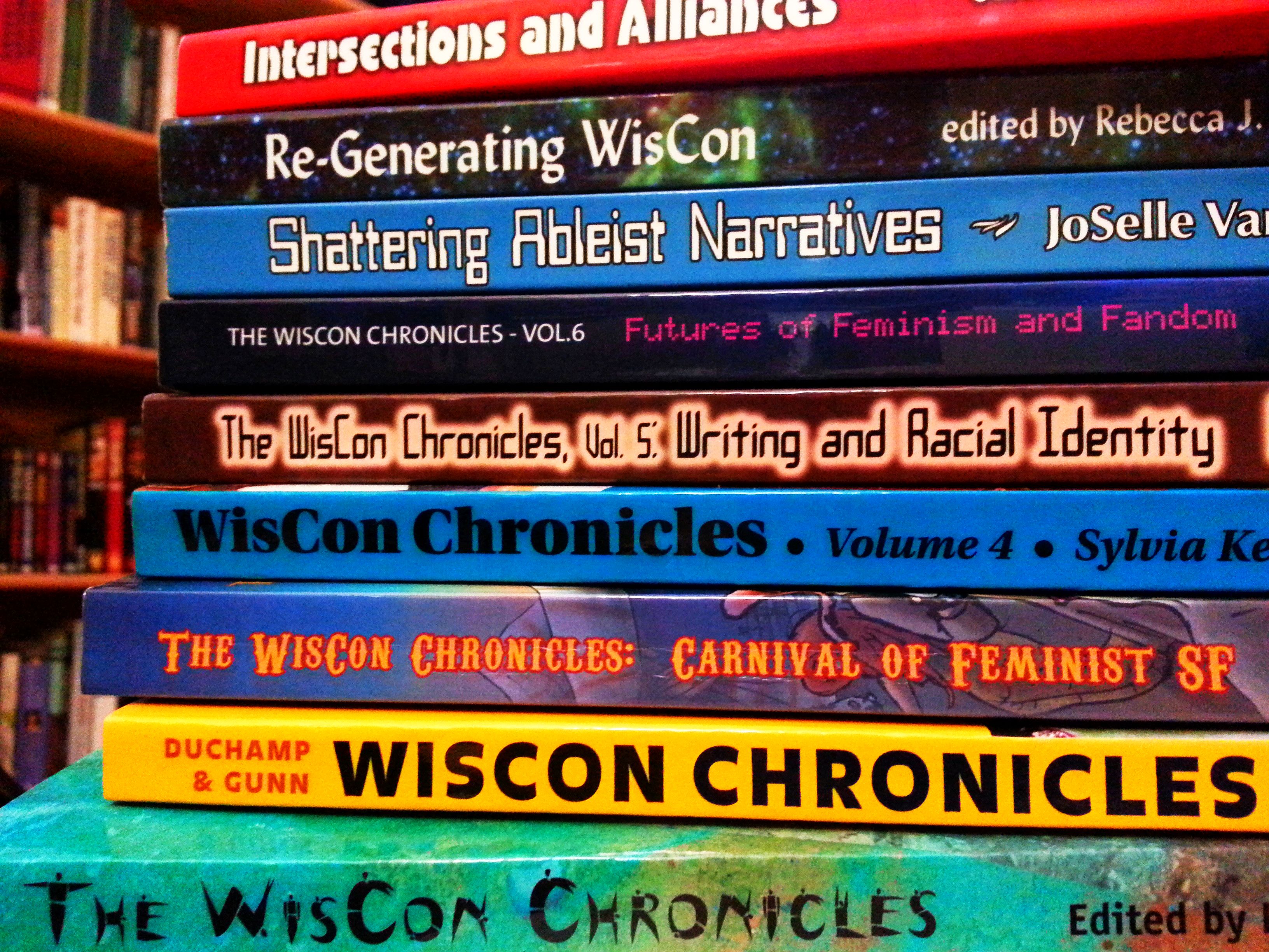 a stack of all volumes of the WisCon Chronicles -- 9 books with colorful spines