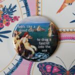 Image of a button with the words "feels like a good day to drag a fascist into the sea" over a painting of mermaids