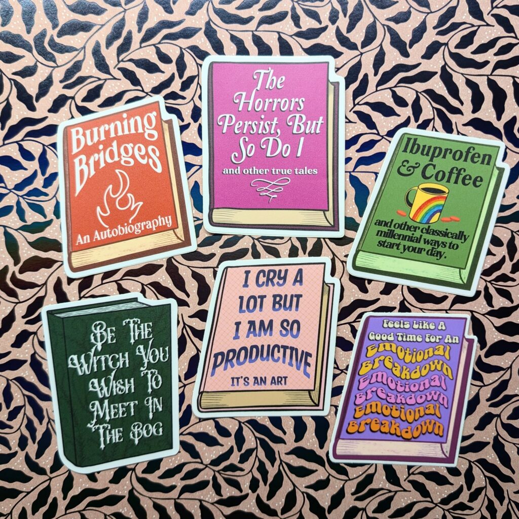 Six book-shaped stickers. "Burning Bridges: An Autobiography," "The Horrors Persist But So Do I," "Ibuprofen & Coffee and other classically millennial ways to start your day," "Be the Witch You Wish to Meet in the Bog," "I Cry a Lot but I Am So Productive," Feels Like a Good Time for an Emotional Breakdown"