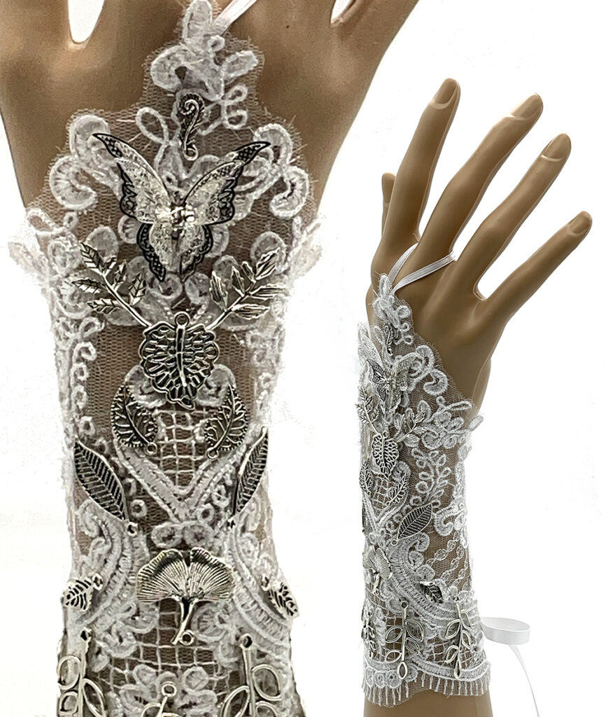 Photo of two hands wearing a white lace sleeve that extends in a point over the hand, decorated with silver metal charms.